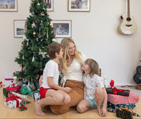 Woman and two children sitting on the floor in front of a Christmas tree with presents. Tis the Season Xmas Prints. Festive Kit.